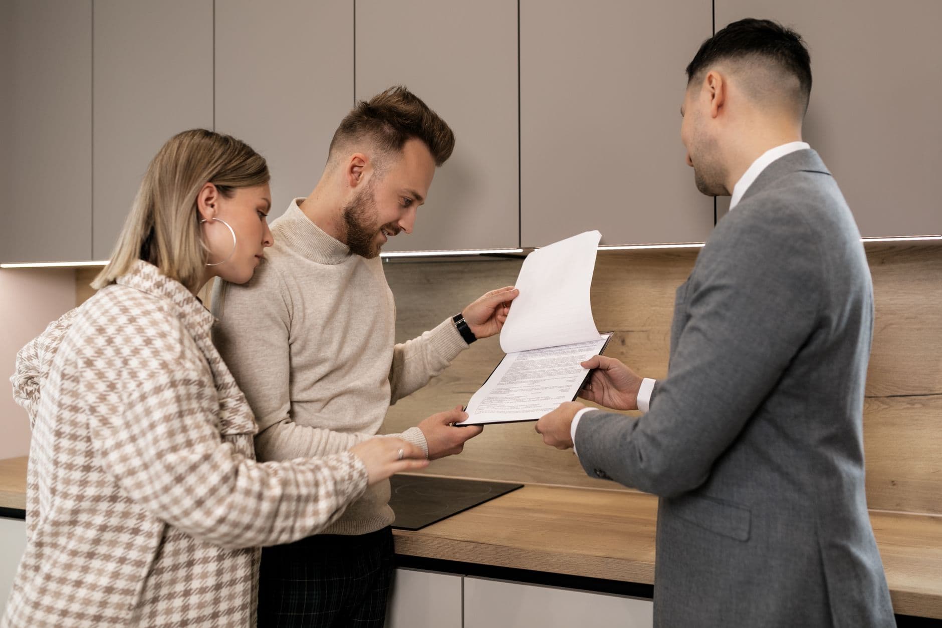 Ein Paar prüft Immobilienunterlagen mit einem Makler in einer modernen Innenumgebung und diskutiert einen potenziellen Immobilienkauf.